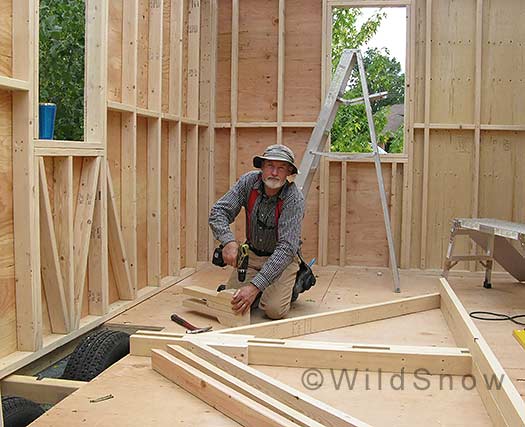Roof is a classic square gable, meaning it's 45 degrees. That'll shed snow and make a good kicker when the snow gets deep. In this photo I'm framing the gable ends for a 'ladder' style eave/overhang, which is the stronger way to frame such a thing (need to consider that possible 150psf snowload!).