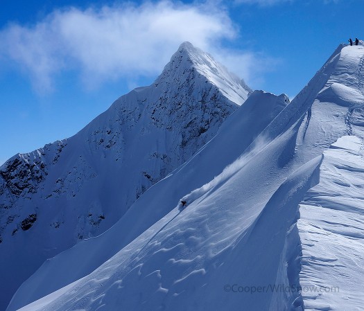 Tyler Wilkes laying out a bottomless turn off the ridge above camp. The White Fang looms in the background.