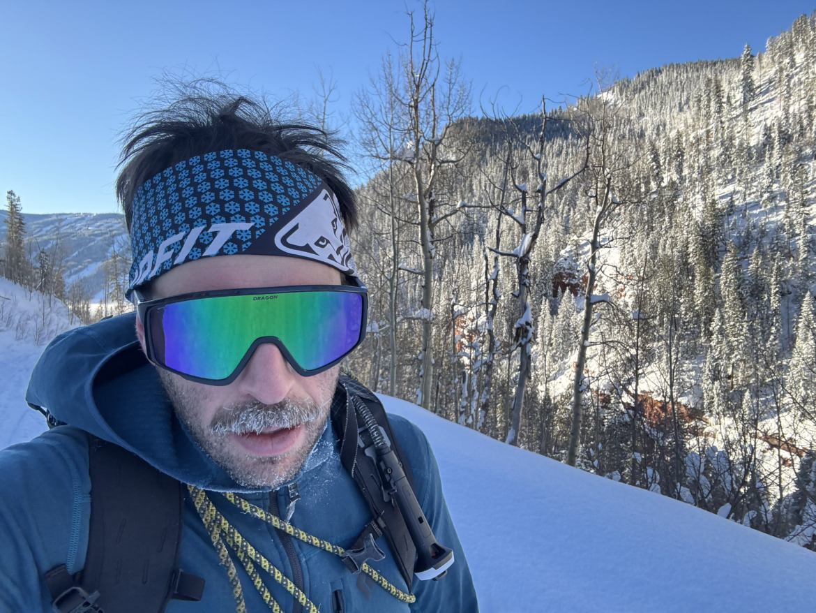 close-up of skier in headband wearing a mustache and ski touring sunglasses