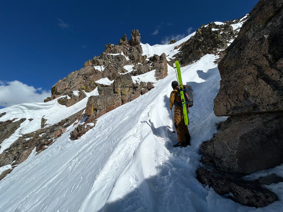 backcountry skier with skis on his back climbing a rocky snowy area