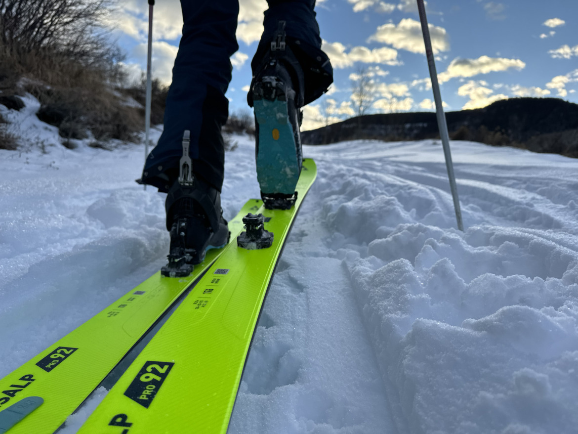 low-angle view from behind of skier touring uphill in neon yellow skis