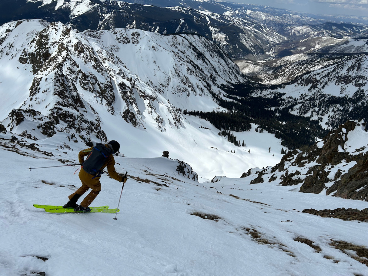 backcountry skier skiing away from the camera with mountains in background