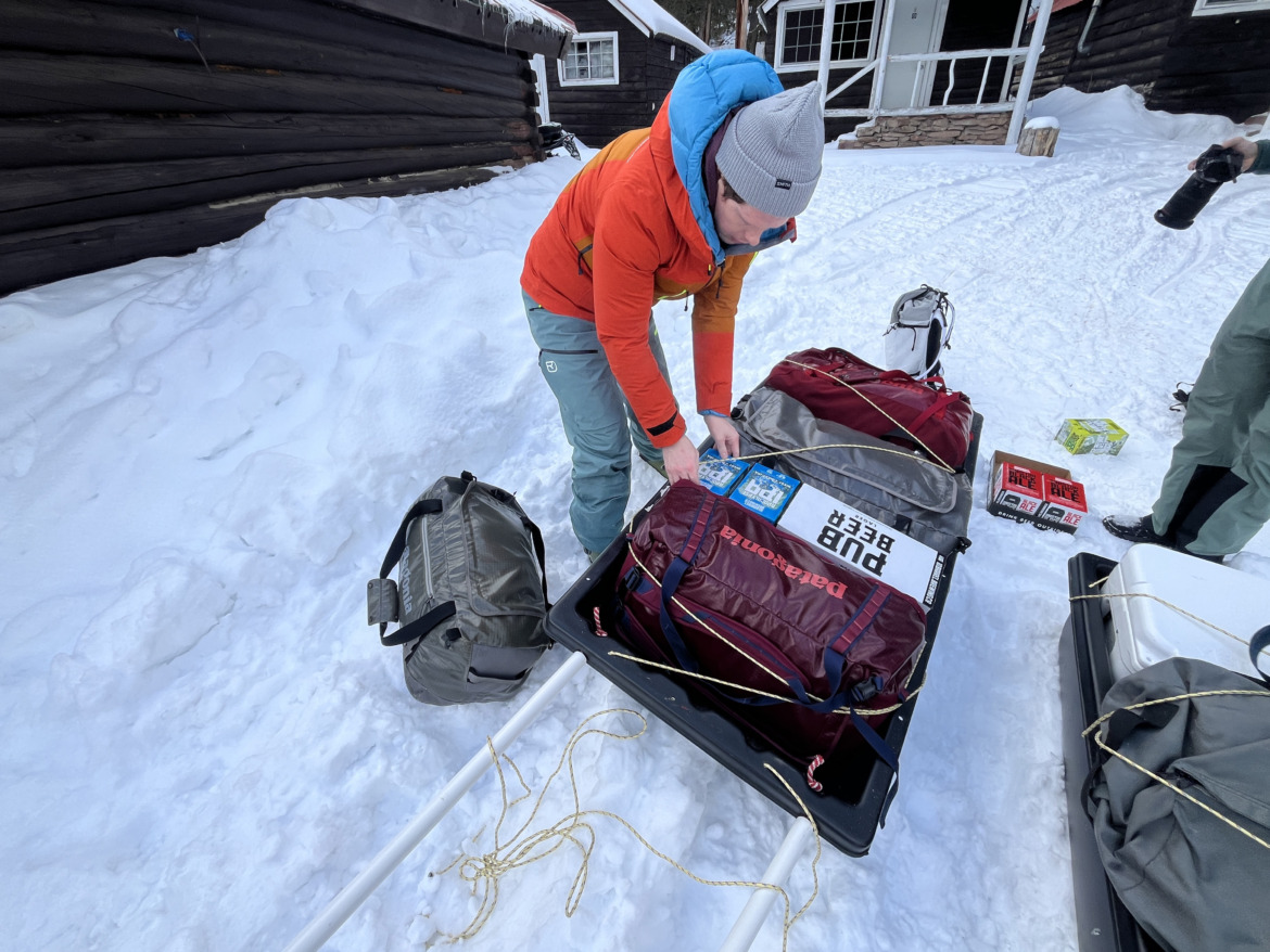 man loading a pulk for dragging into a backcountry ski hut