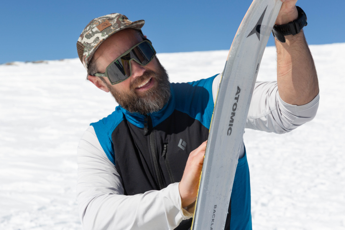 Man applying ski touring skins to his skis wearing sunglasses and a hat
