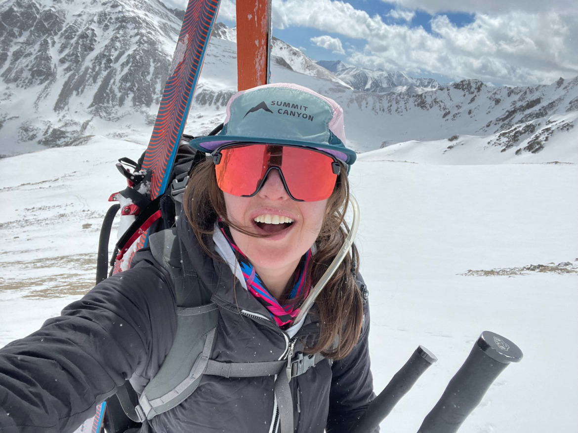 female skier wearing Smith Bobcat ski touring sunglasses with skis on her back and holding ski poles