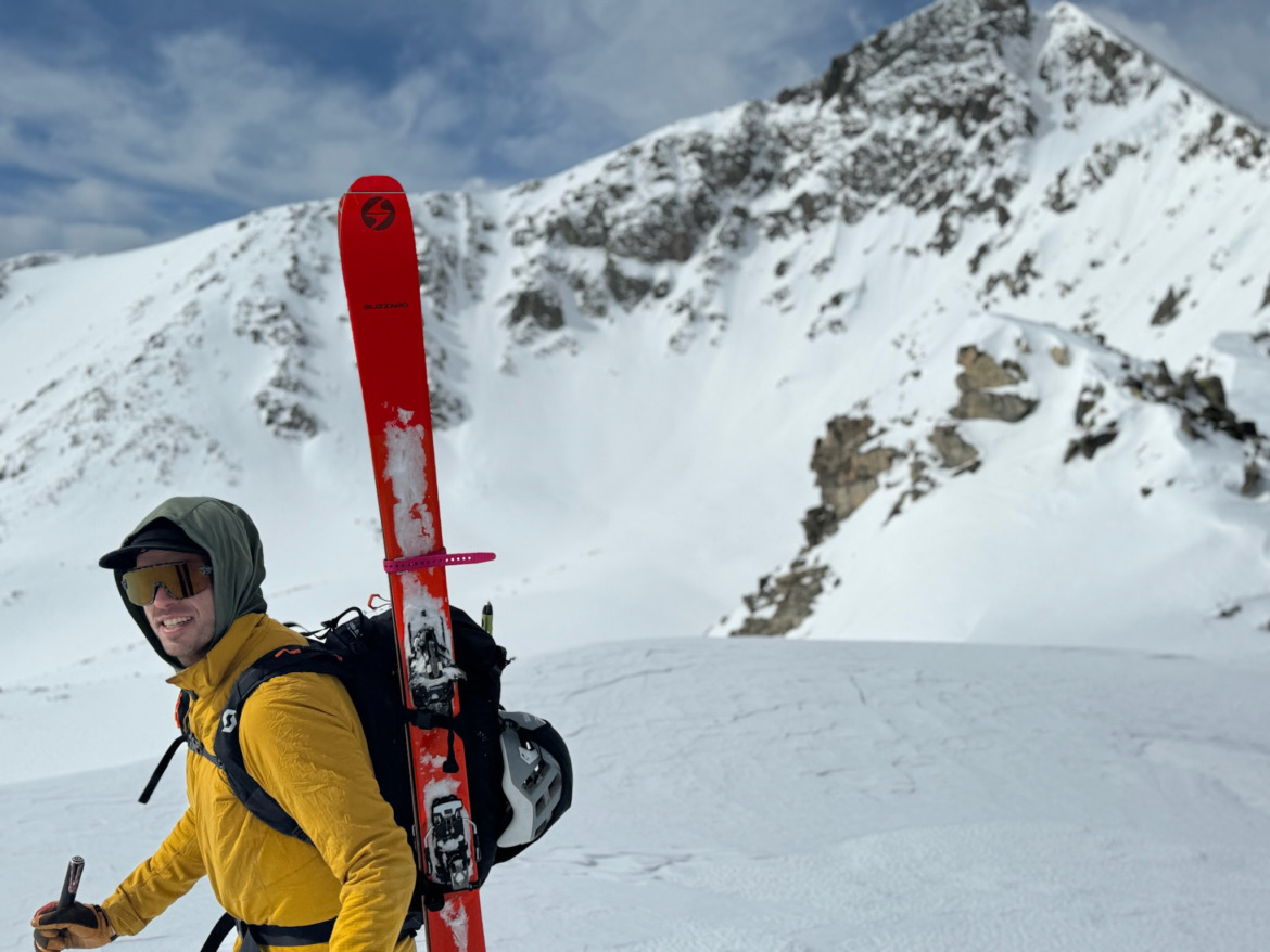 skier wearing touring sunglasses with skis on his back in the mountains