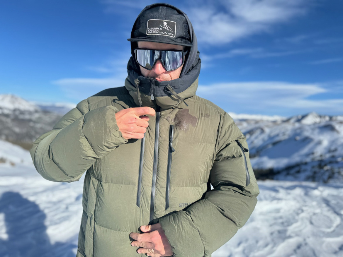 backcountry skier zipping up his coat wearing a cap and touring sunglasses