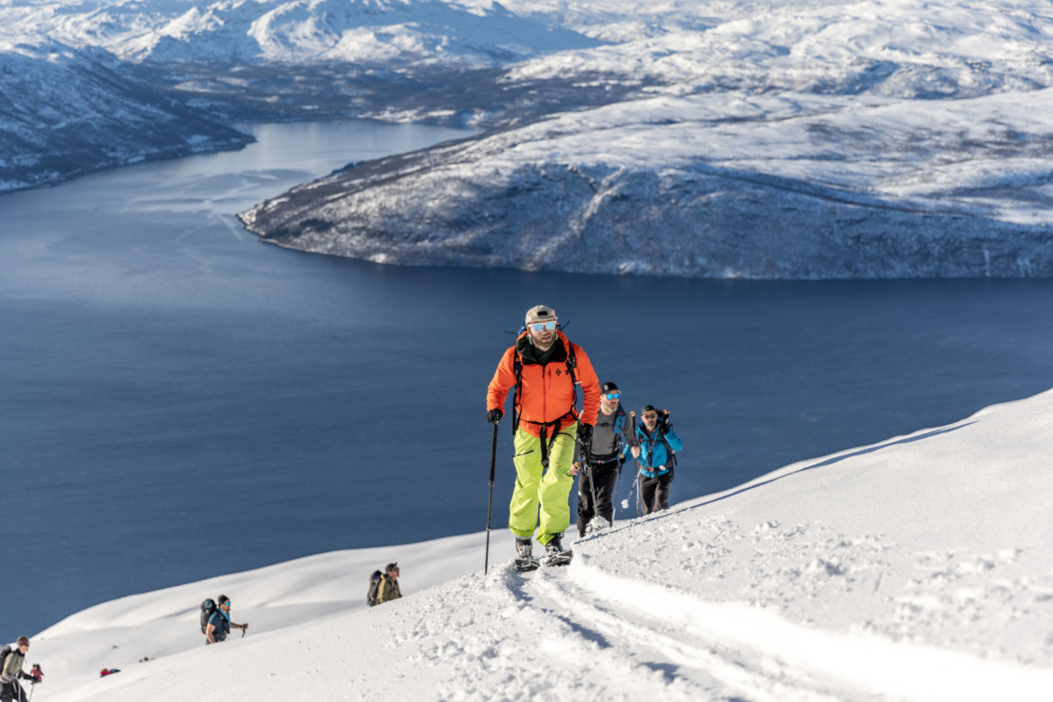 Splitboarder heading uphill in Norway with colorful outerwear and Wolverine Split Sticks in hand