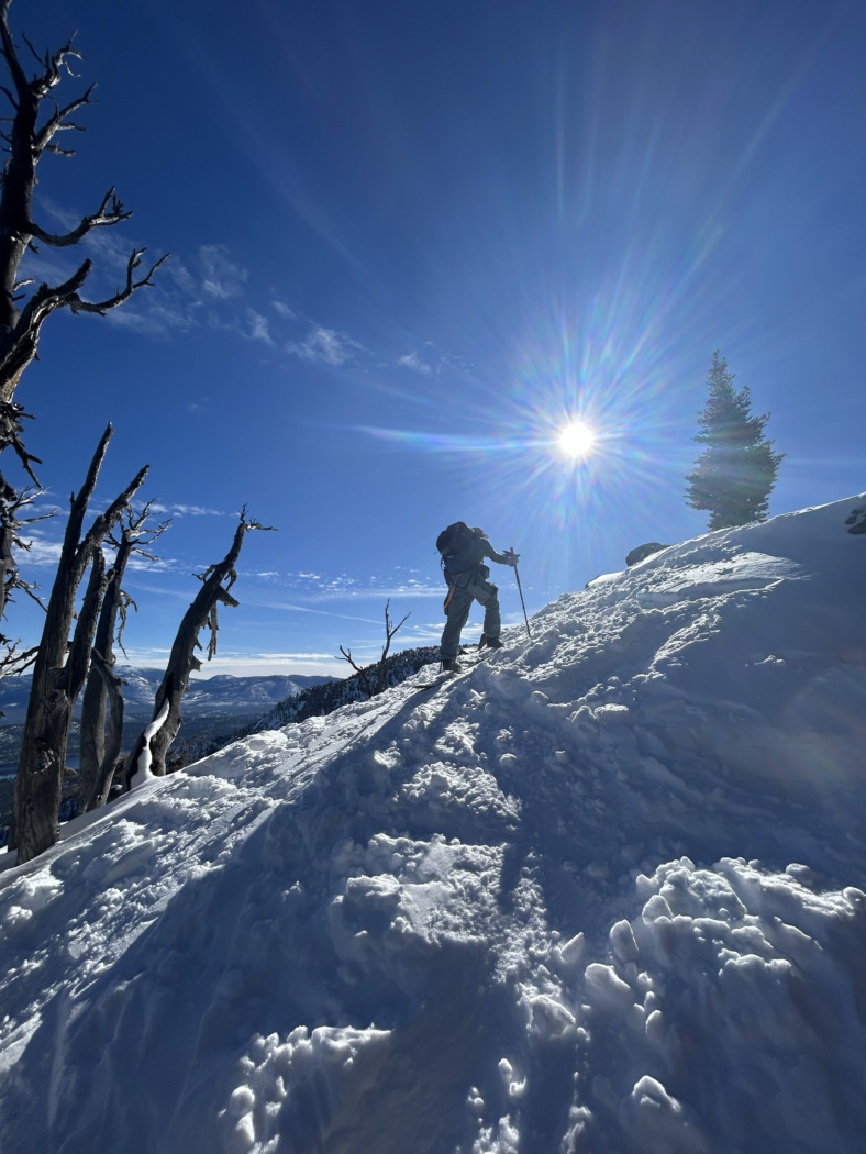 skiers backlit hiking uphill on a ridgeline