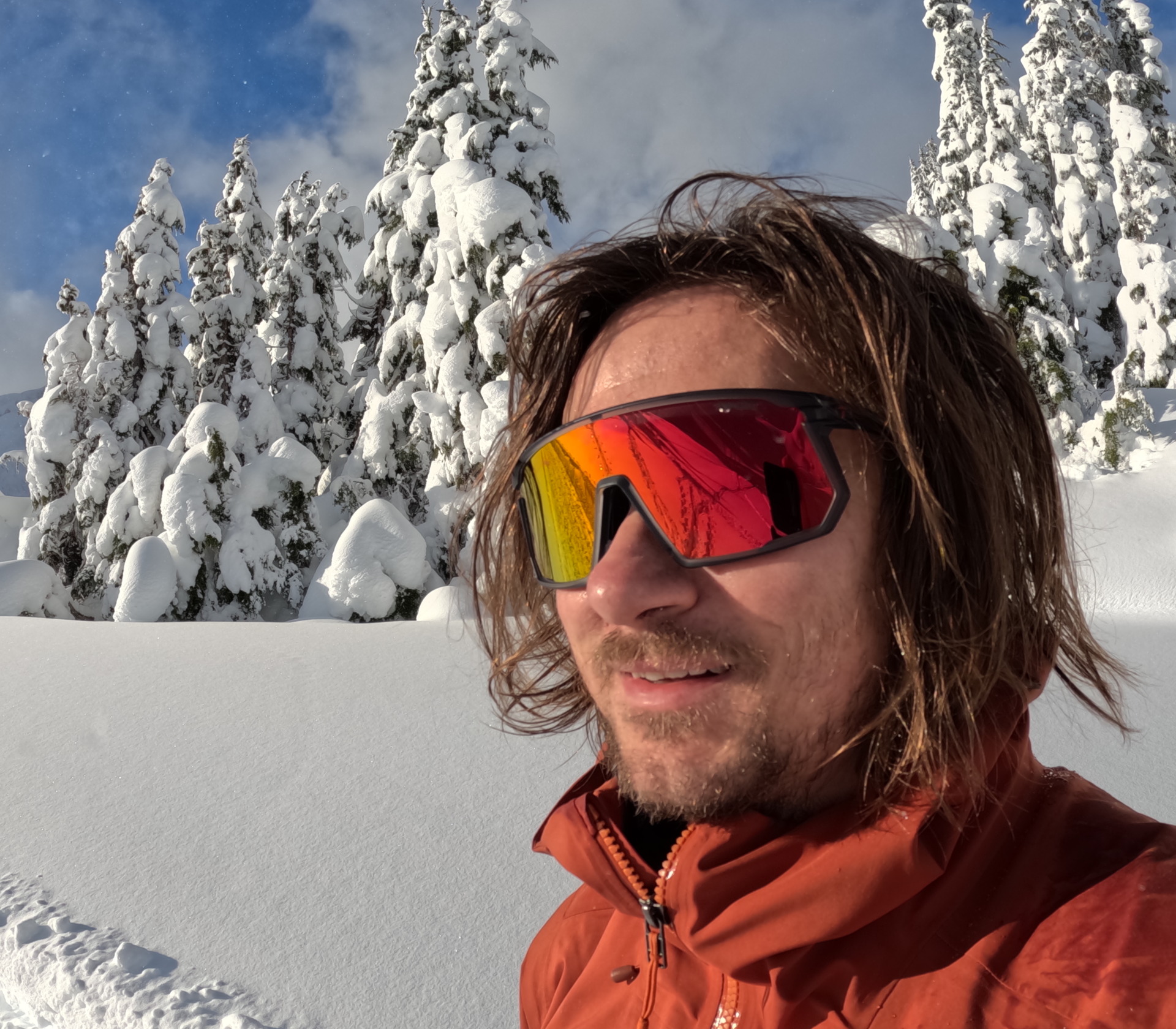 man with long hair in oversized sunglasses in a snowy field with trees