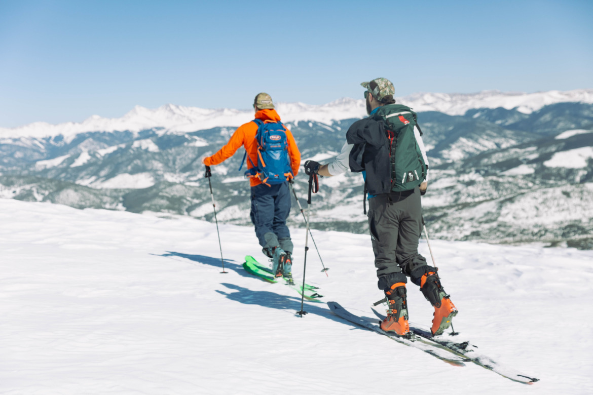 two backcountry skiers on a ridge skinning away from camera wearing backpacks